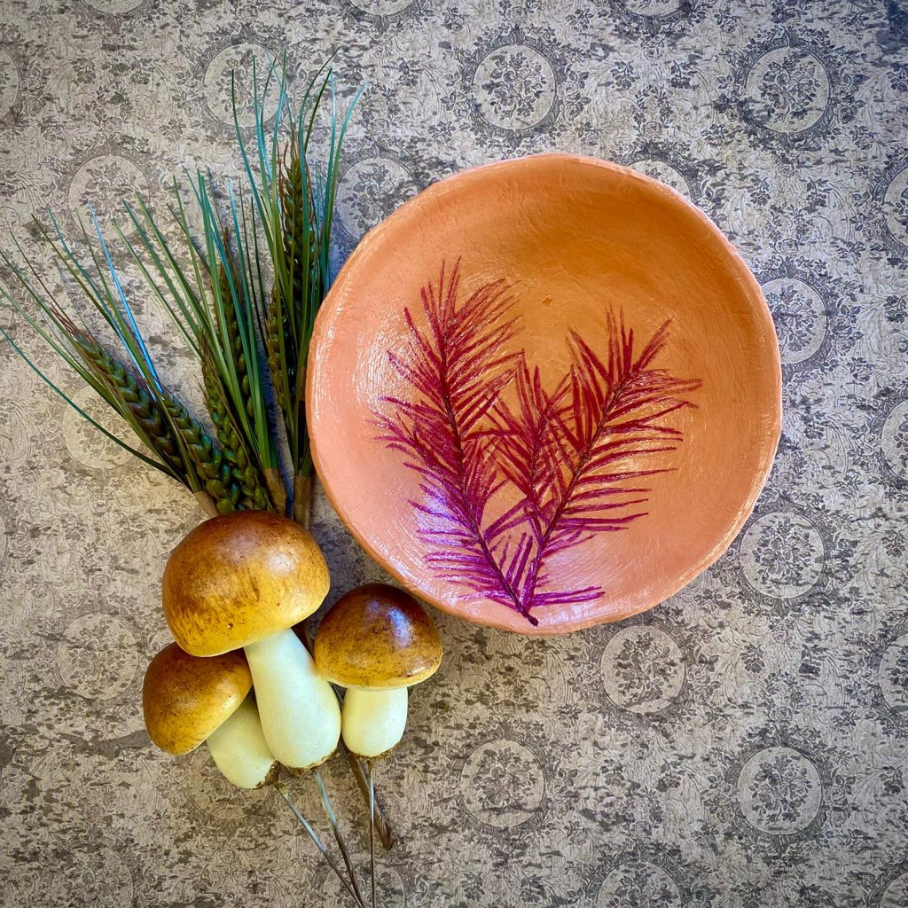Ein Tonschälchen mit einer Verzierung und herbstliches Dekomaterial
